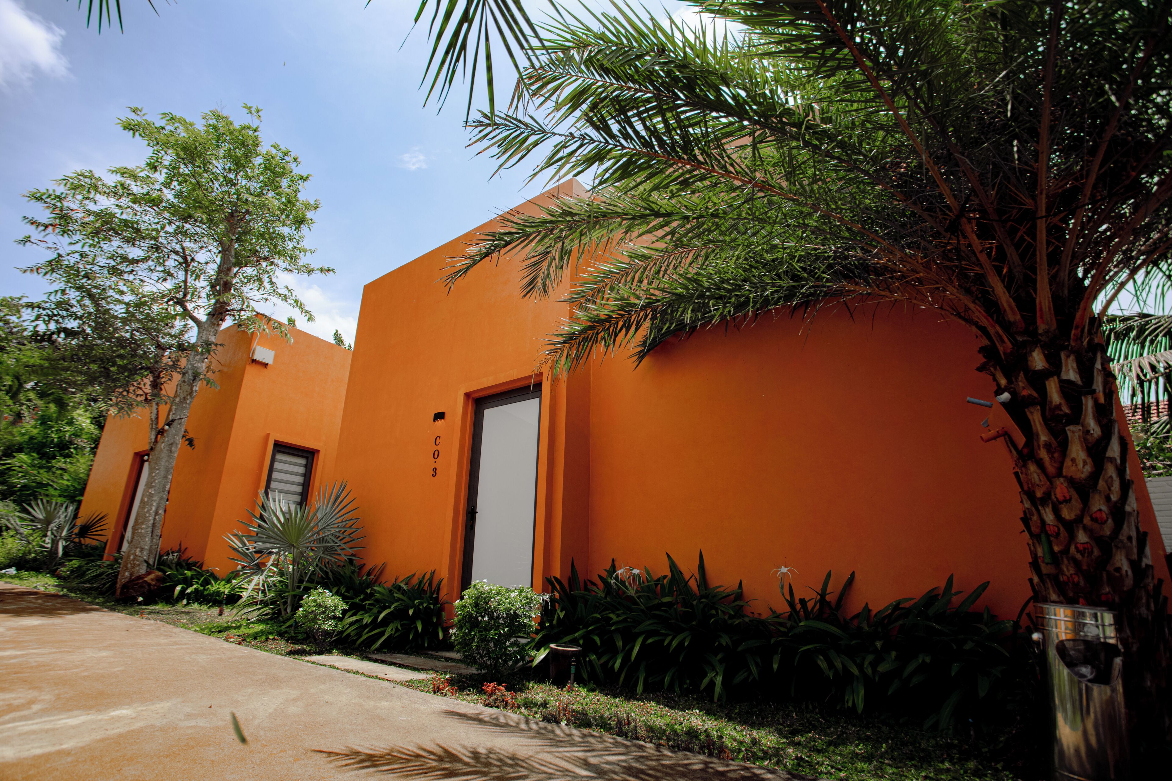 A building with a bright orange facade, a door, and surrounding greenery.