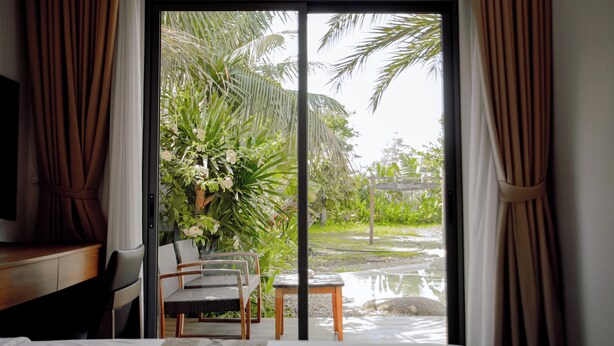 A room with a bed, a desk, a chair, and a view of a garden through a sliding door.