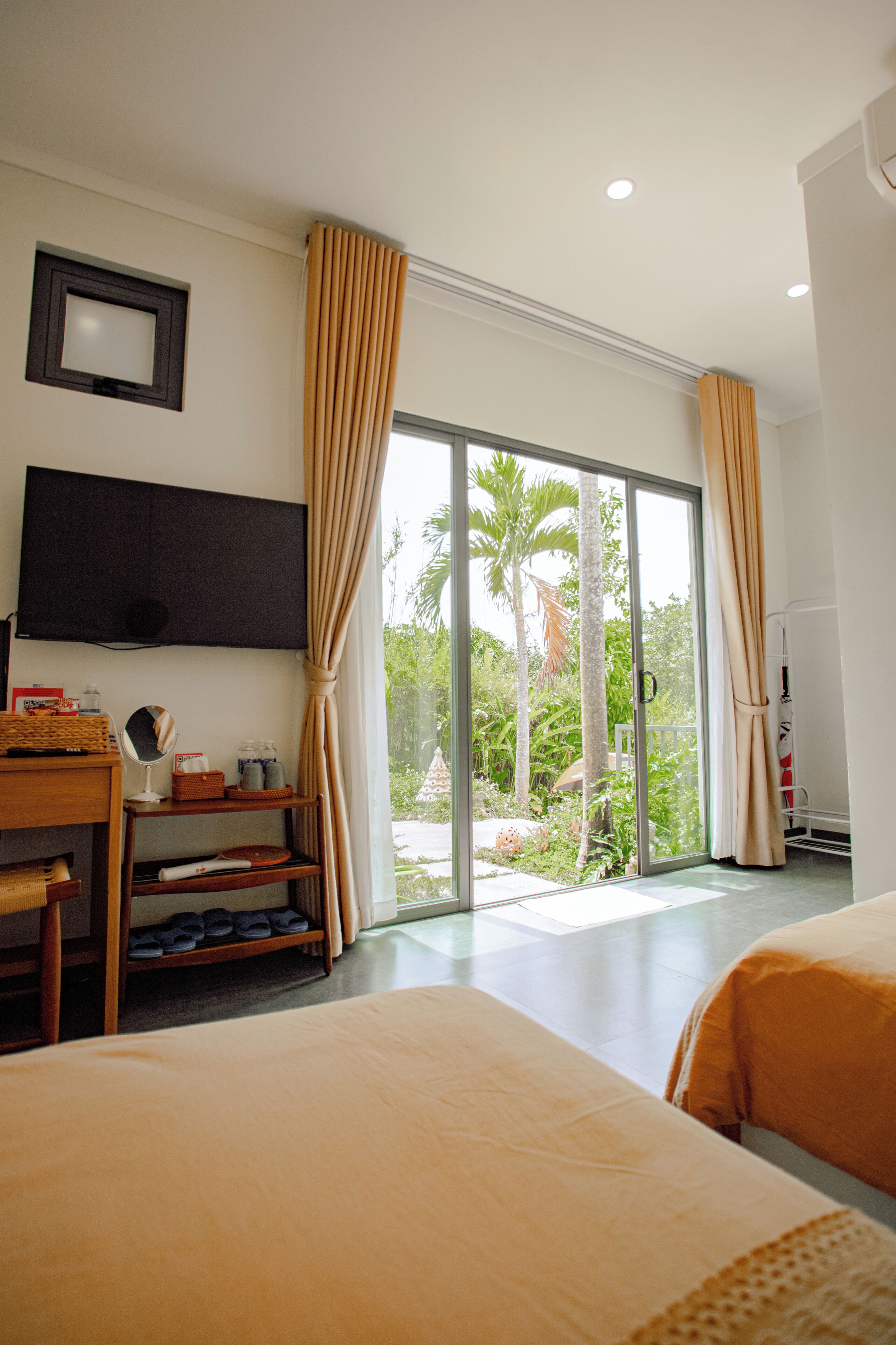 Camera d'albergo con un letto, una scrivania, un televisore e una porta scorrevole con vetro esposta su un giardino.