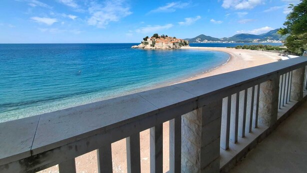 A coastal view with a clear blue sky, a sandy beach, and a small island with buildings. - Beachfront Four bedroom Apartment (Sveti Stefan)