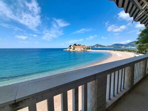 A coastal view with a clear blue sky, a sandy beach, and a small island with buildings. - Beachfront Four bedroom Apartment (Sveti Stefan)