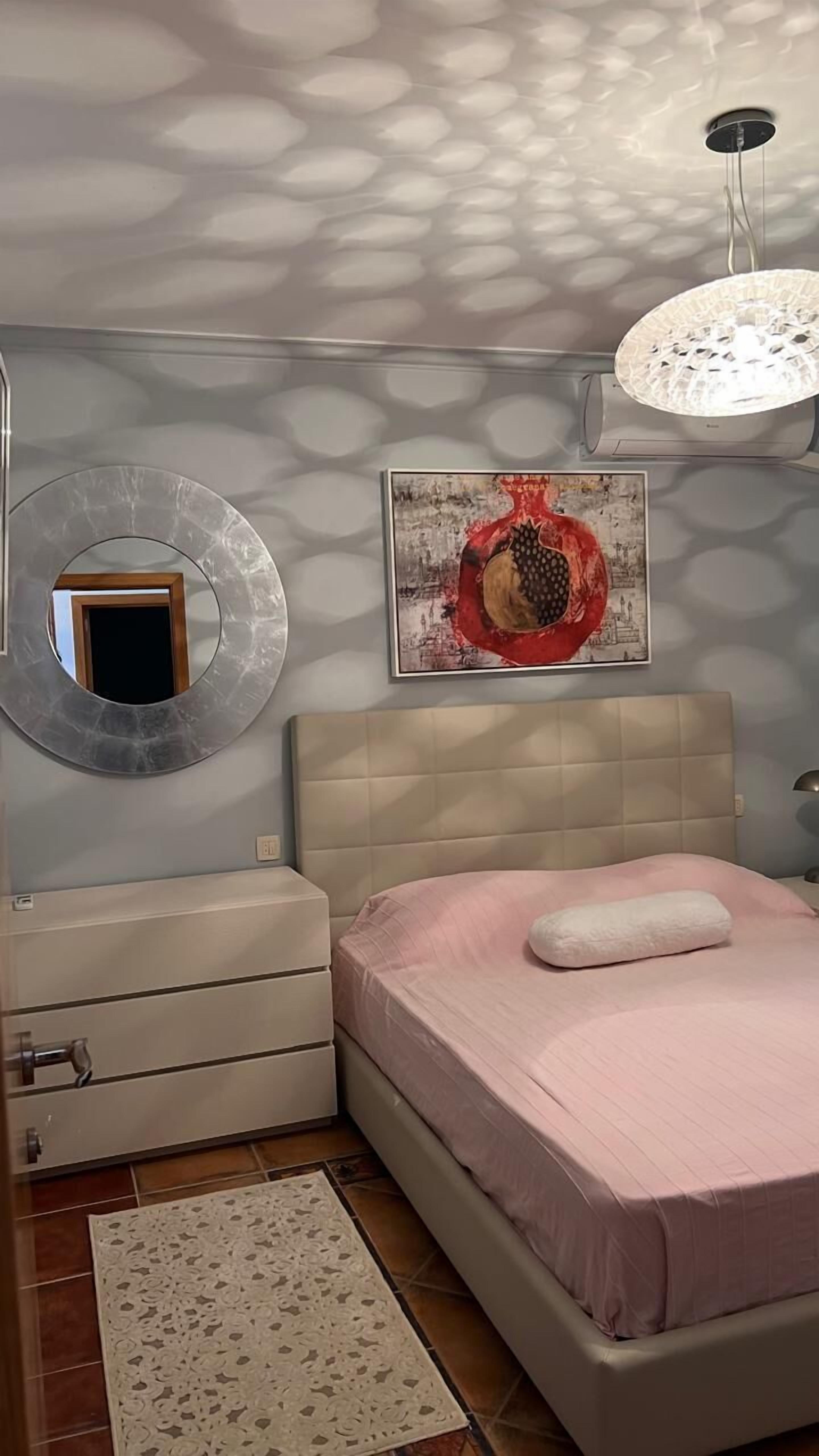 A bedroom with a bed, a dresser, a mirror, a ceiling light fixture, and a wall art piece.