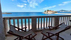 A balcony with two wooden lounge chairs facing a beach and a small island. - Beachfront Four bedroom Apartment (Sveti Stefan)