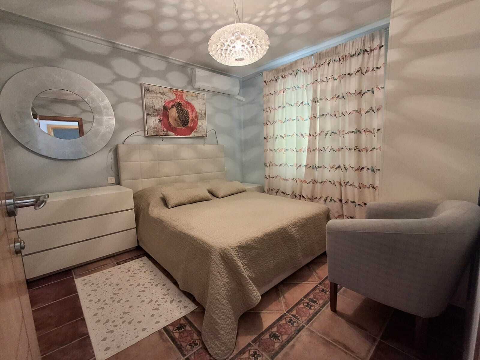 A bedroom with a bed, a chair, a dresser, a mirror, and a ceiling light fixture.