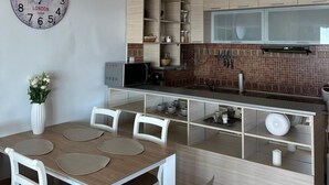 A modern kitchen with white cabinetry, a dining area with a wooden table and white chairs, and a decorative clock on the wall. - Beachfront Four bedroom Apartment (Sveti Stefan)
