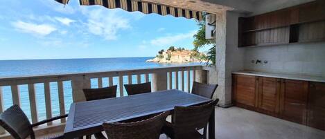 A balcony with a table and chairs, overlooking a coastal view.
