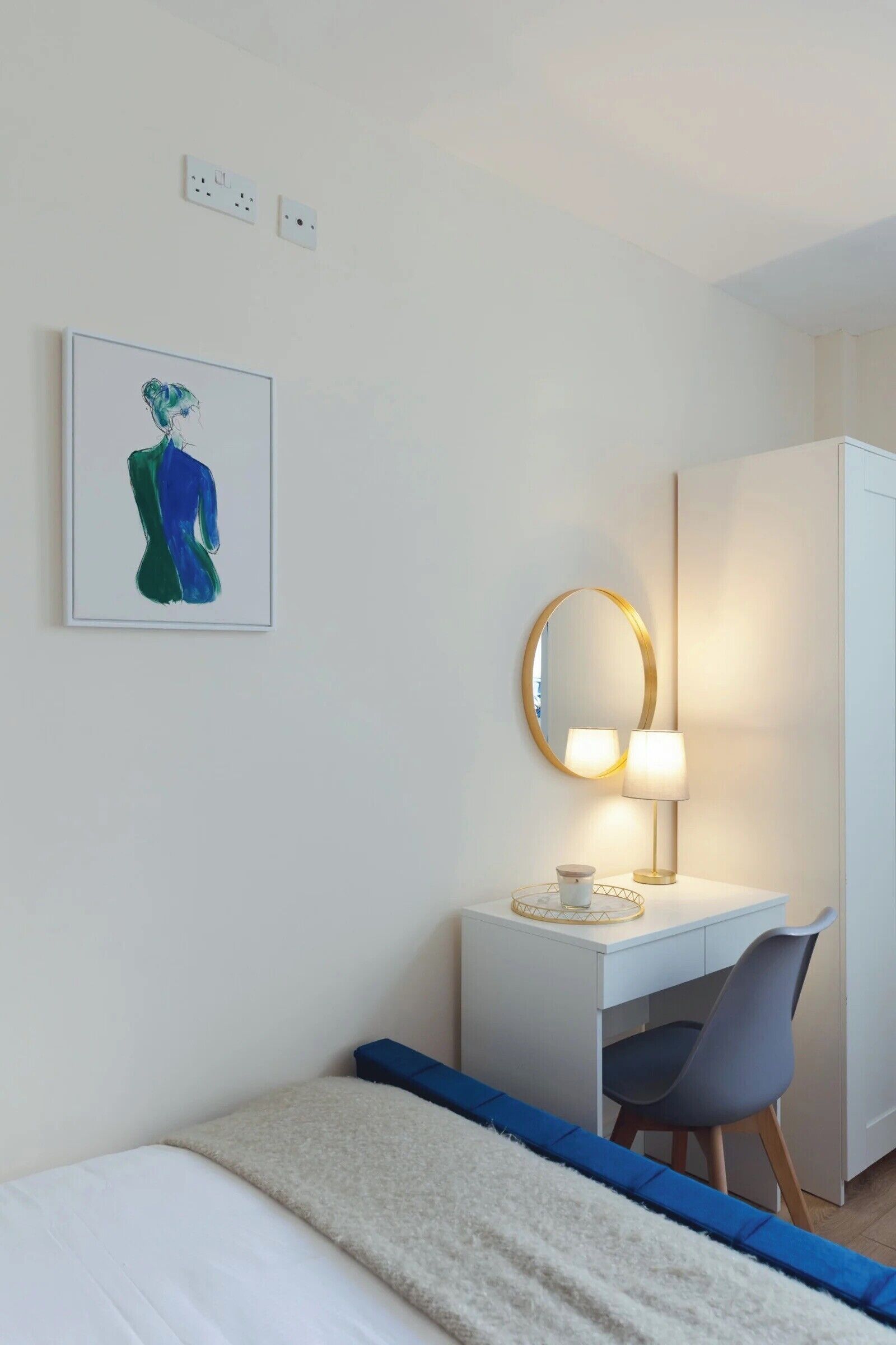 A bedroom with a bed, a desk with a chair, a mirror, and a lamp.