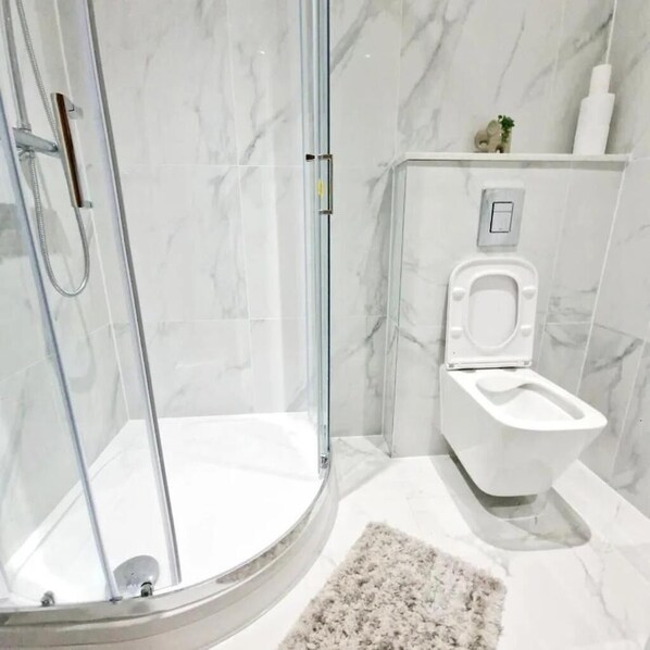 A bathroom with a glass shower enclosure, a white toilet, and a marble floor. - Crendon House Cosy Studio - Sleeps 2 & Kitchen (High Wycombe)