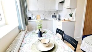 Una cucina compatta con mobili bianchi, un forno a microonde e un piccolo angolo ristoro con un tavolo apparecchiato per due.