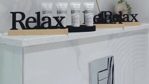 Un bagno con parete in marmo, uno scaffale con articoli da toilette e un cartello con scritto 'Relax'.