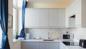 Una cucina compatta con mobili bianchi, un forno a microonde, un tostapane e un lavello.