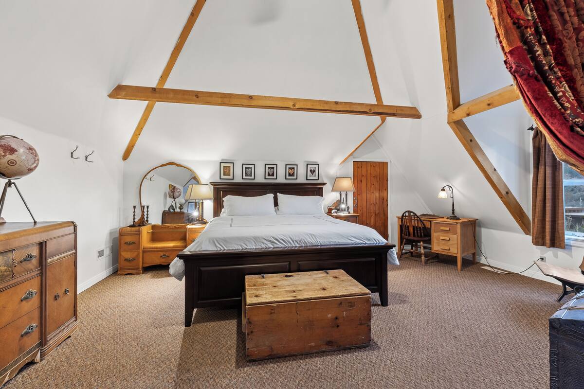 Een slaapkamer met een groot bed, houten balken, een dressoir, een kast, een bureau en een raam met gordijnen.