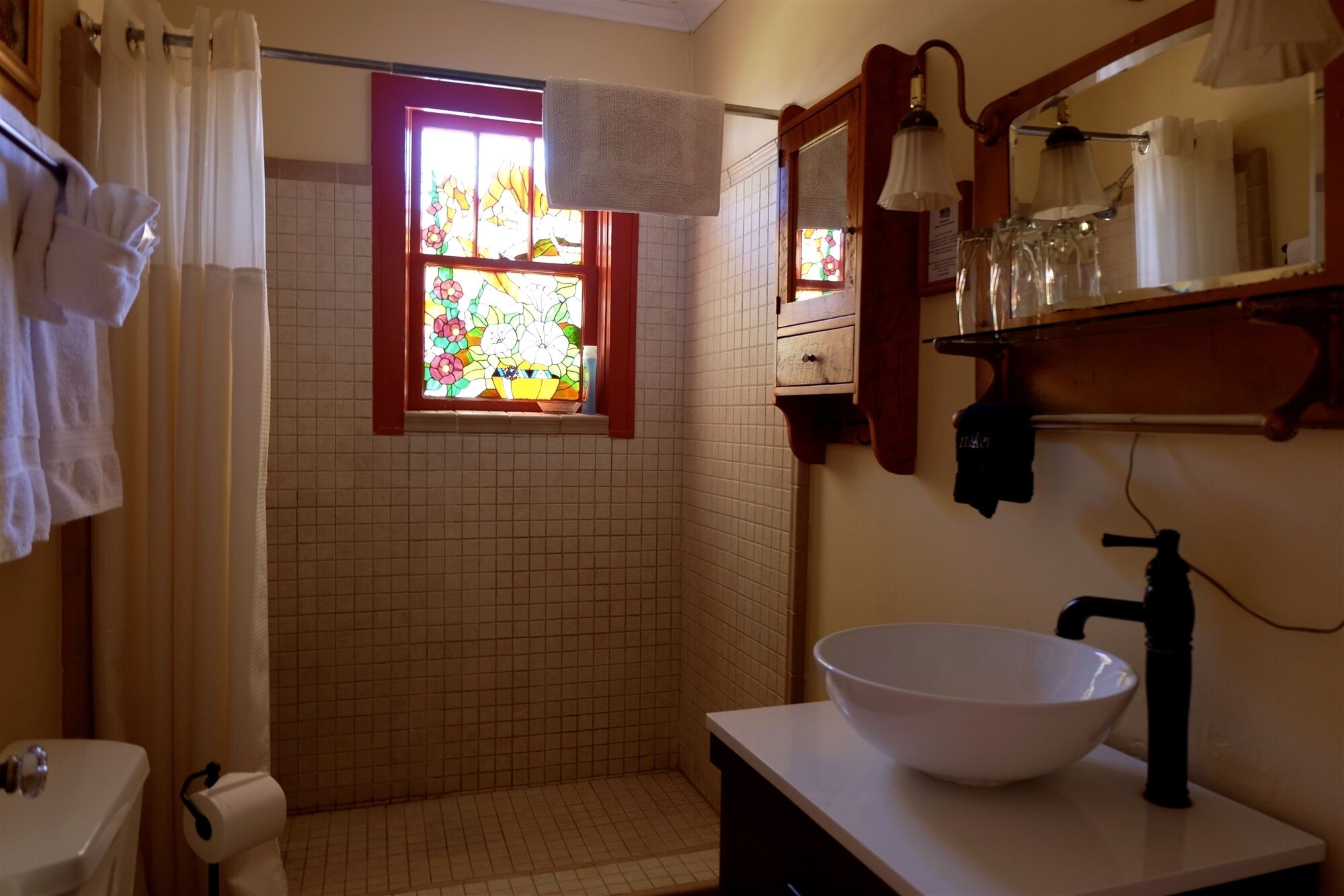 Un baño con un lavamanos blanco, un ventanal con vidrieras y una cortina de ducha.