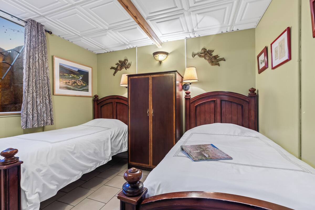 Een kamer met twee eenpersoonsbedden, een kledingkast, een nachtkastje met een lamp en een lijst aan de muur.