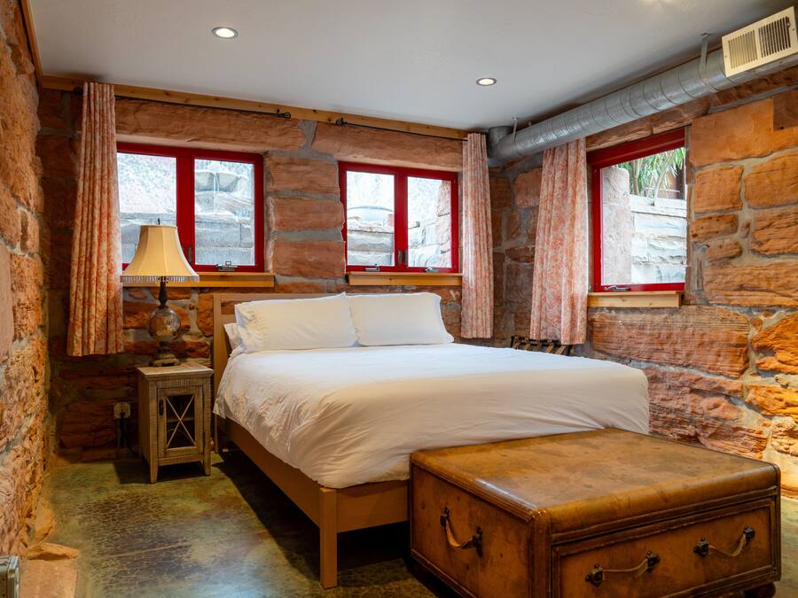 A bedroom with a wooden bed, stone walls, and two windows with red frames.