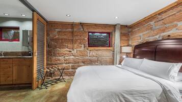 A bedroom with a stone wall, wooden headboard, and a bed with white bedding.