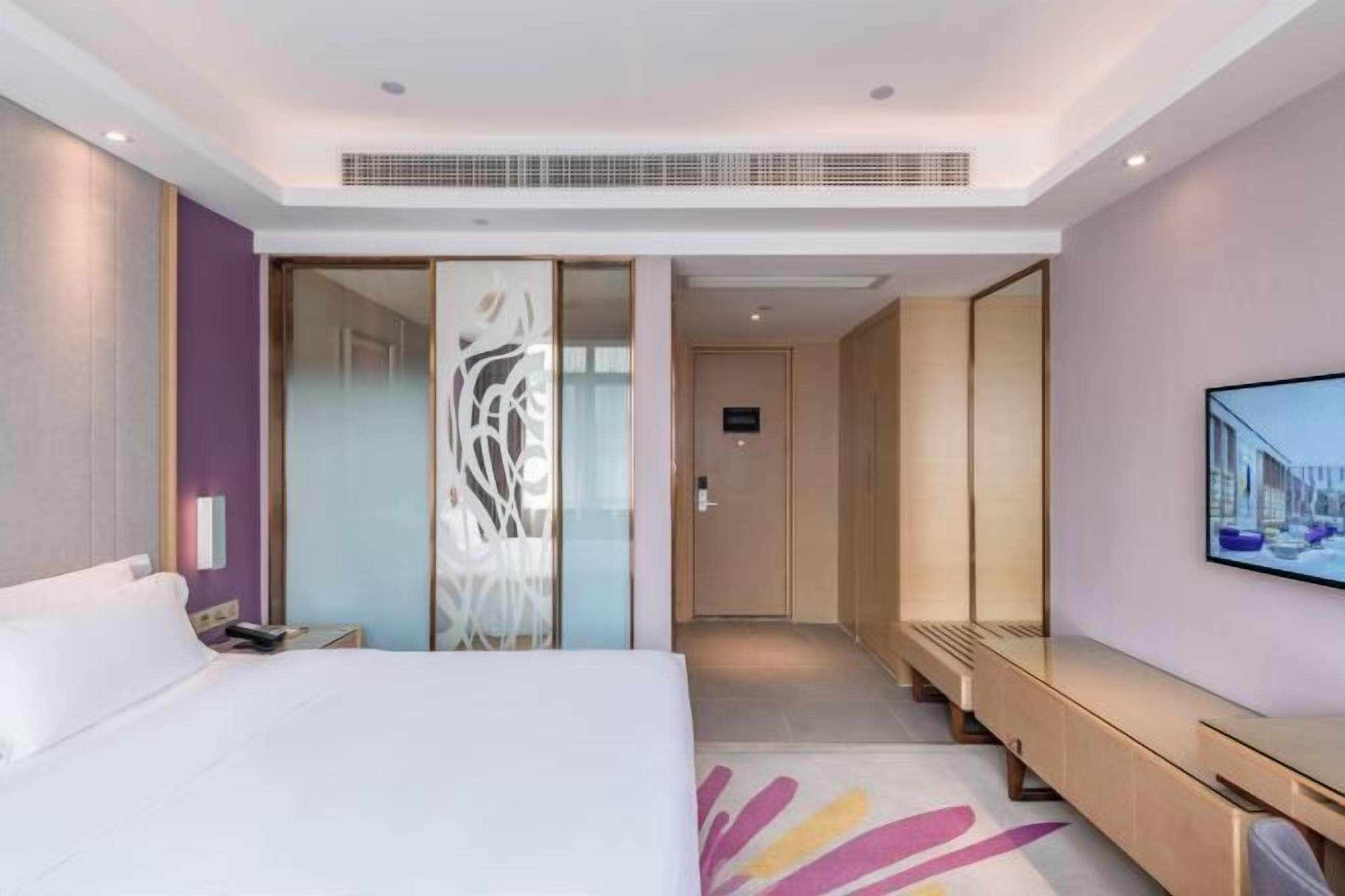 Ein modernes Hotelzimmer mit einem großen Bett, einem begehbaren Kleiderschrank, einer Sitzecke und einem an der Wand befestigten Fernseher.