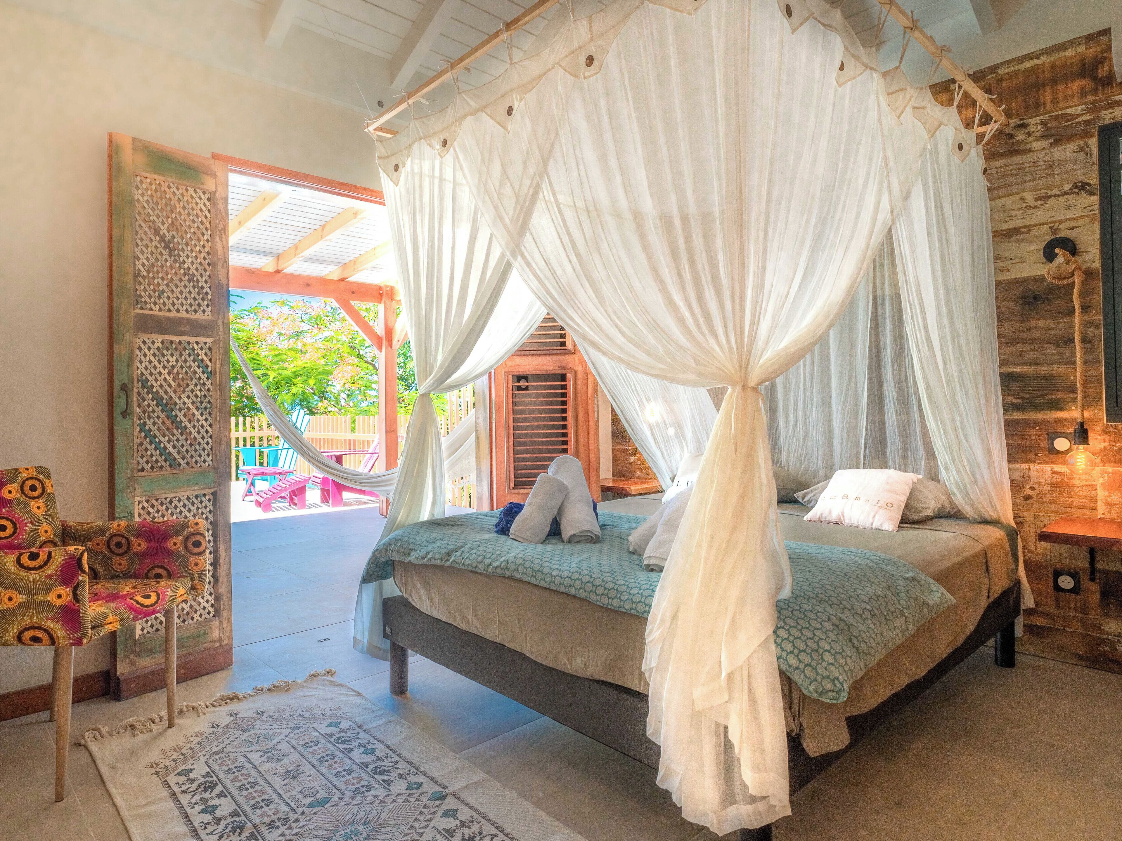 A bedroom with a four-poster bed, a wooden door, and a view of the outside.