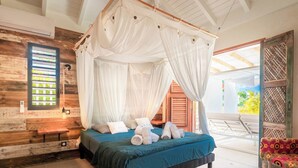 Ein Bett mit Baldachin und Himmelblauem Bettbezug, eine Sitzbank und ein gemustertes Teppich in einem Raum mit Holzwänden und einem großen Fenster.