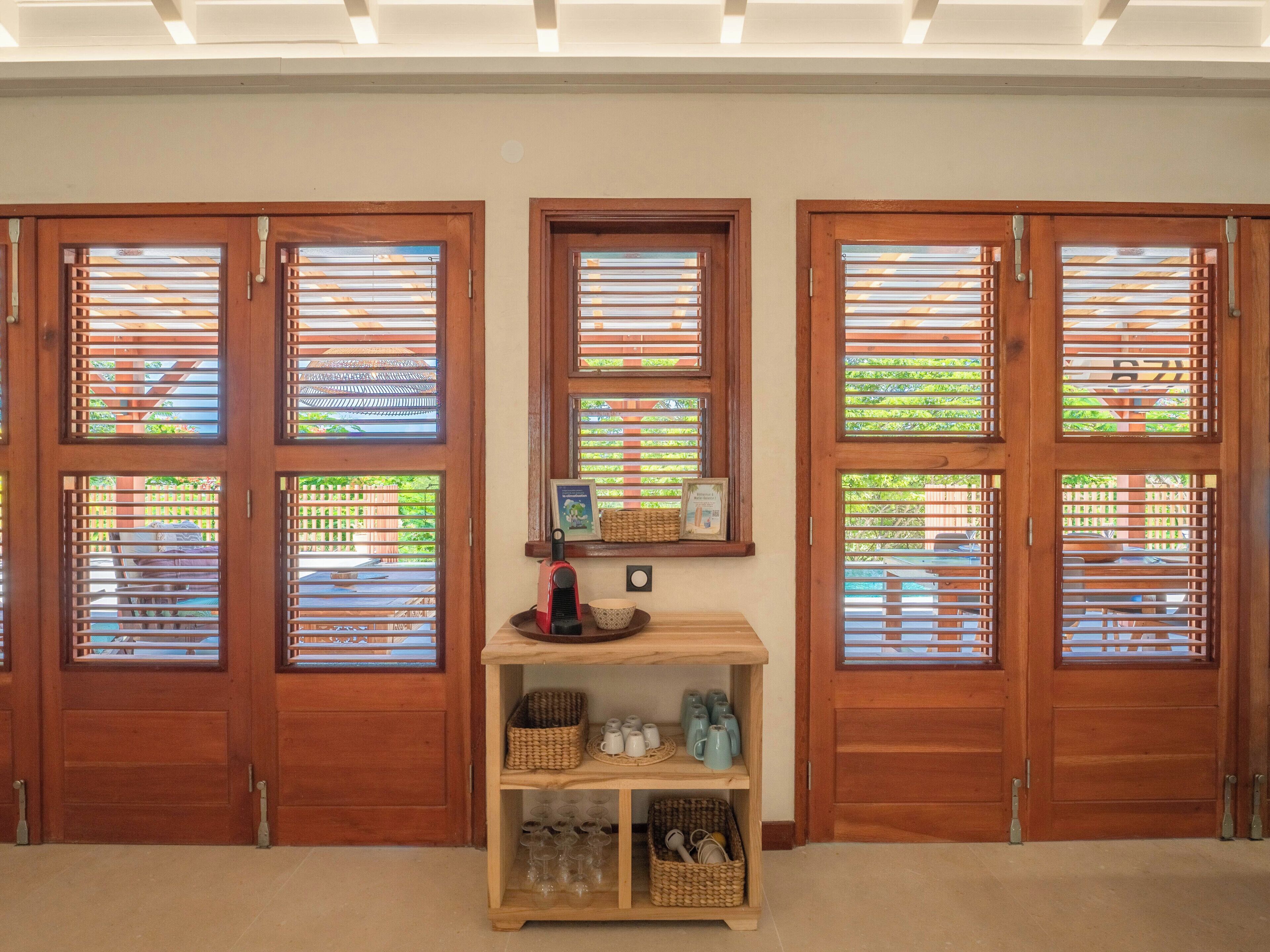 A room with three wooden doors, each with a window featuring horizontal blinds. A small wooden shelf with various items is placed between the doors.