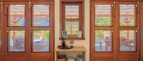 A room with three wooden doors, each with a window featuring horizontal blinds. A small wooden shelf with various items is placed between the doors.