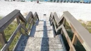 A wooden staircase leading to a beach with a clear view of the ocean.