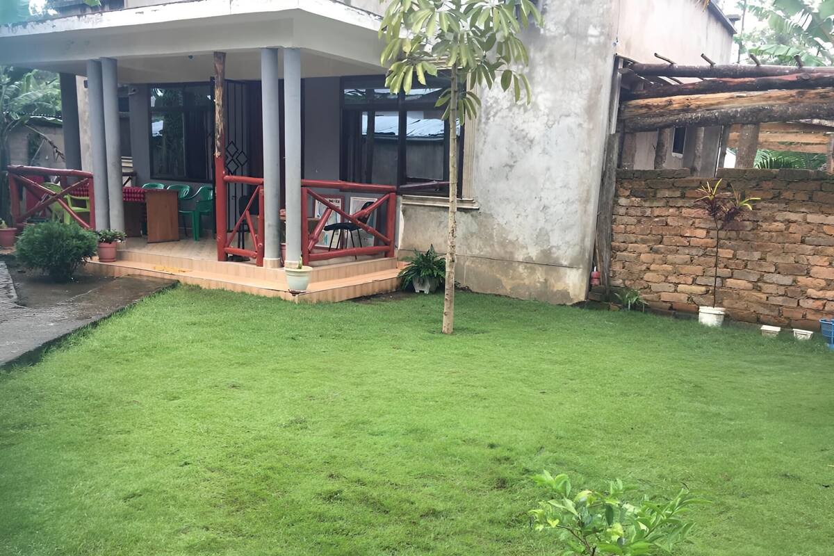 A house with a covered porch, a brick wall, and a small garden area with grass and potted plants.