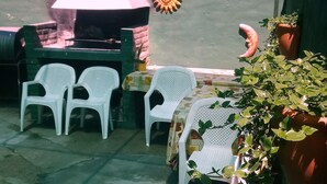 Een buitenpatio met witte plastic stoelen en een tafel, een barbecue en een bloempot.