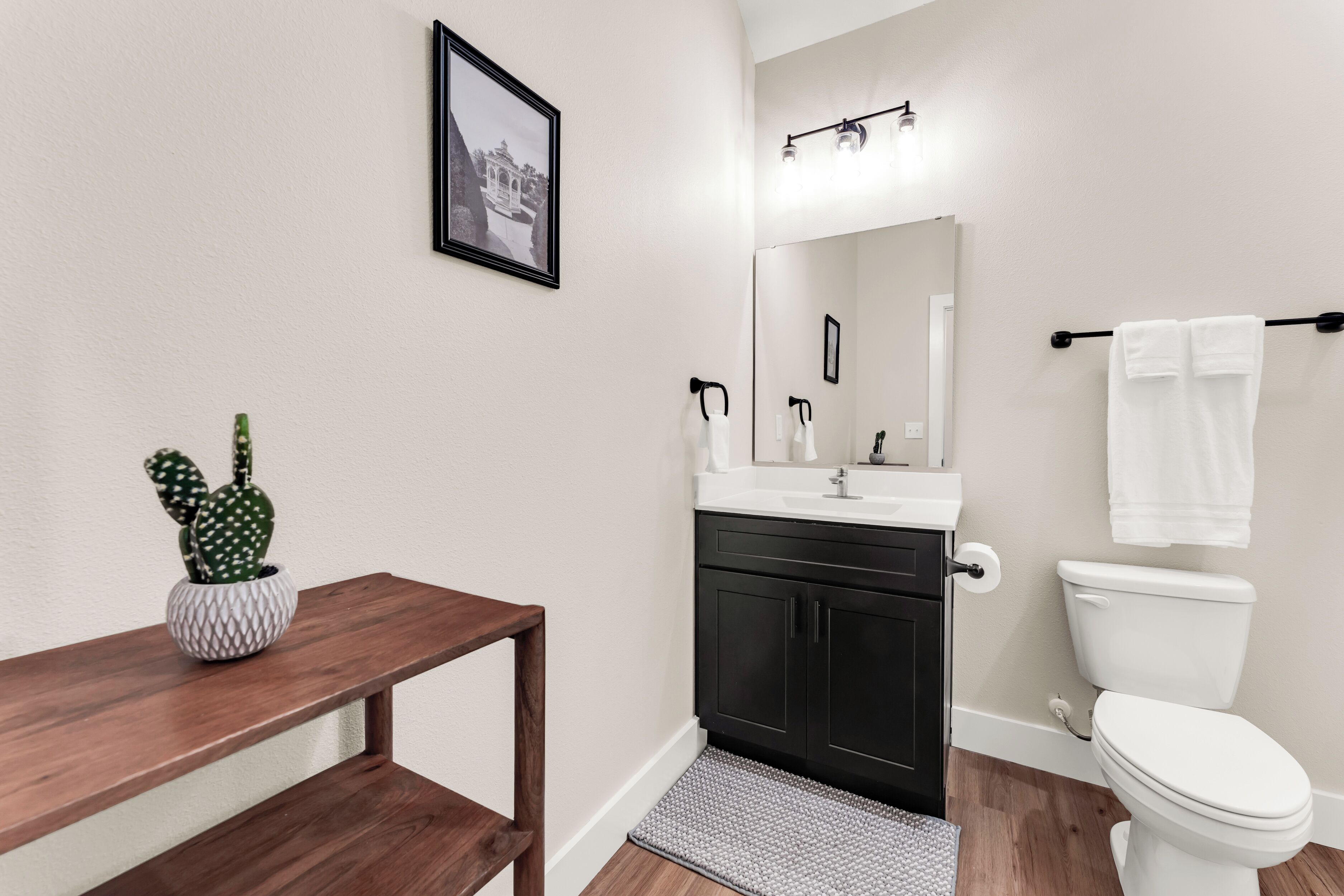 A modern bathroom with a wooden vanity, a white sink, a black cabinet, a white toilet, and a framed picture on the wall.