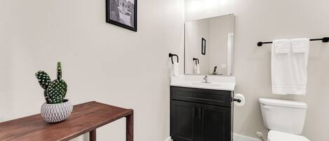 A modern bathroom with a wooden vanity, a white sink, a black cabinet, a white toilet, and a framed picture on the wall.