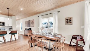 Een moderne keuken met houten kastjes, een centraal eiland met barstoelen en een eetgedeelte met een houten tafel en stoelen.