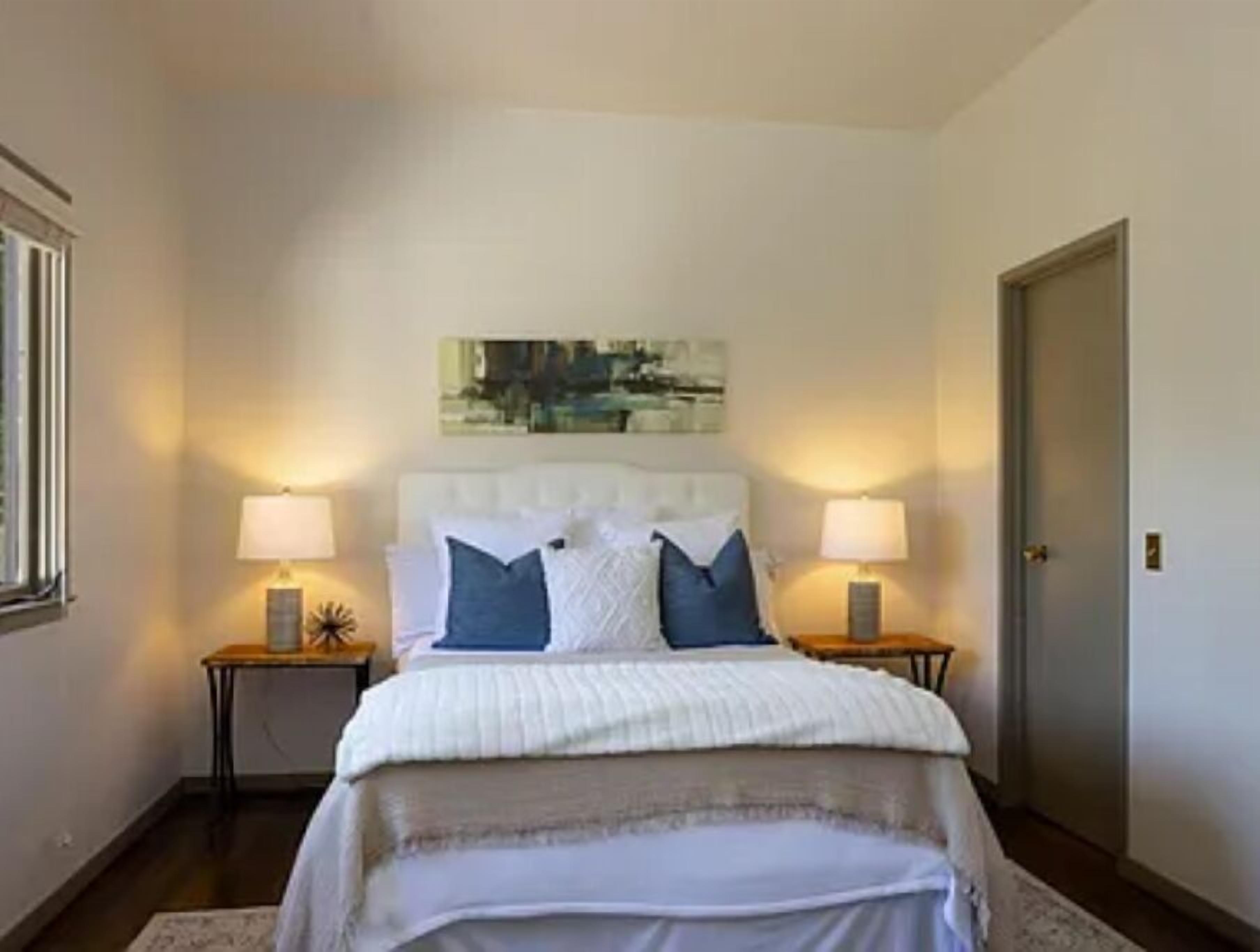 Una camera da letto con un letto grande, due comodini con lampade, una porta e un'opera d'arte appesa al muro.