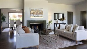 A modern living room with a fireplace, two white sofas, a coffee table, and a large painting above the mantel.