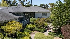 A modern house with a sloped roof, a covered porch, and a well-maintained garden with various shrubs and trees.