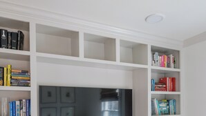 A modern living room with a large flat-screen TV mounted on a white wall, surrounded by white cabinetry and shelves filled with books and decorative items. - Charming Downtown 2 BR Apartment Steps from Downtown Mall (Charlottesville)