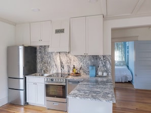 A compact kitchen with white cabinets, a marble backsplash, and a built-in oven.
