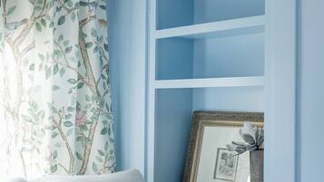 Ein Zimmer mit blauer Wand, einem weißen Sofa mit Blumenkissen und einem gerahmten Bild auf einem Regal.