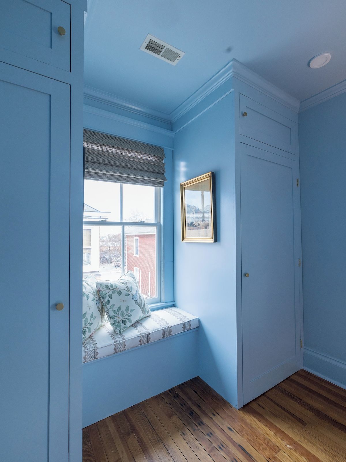 Quarto com um assento junto à janela, um quadro e uma porta.