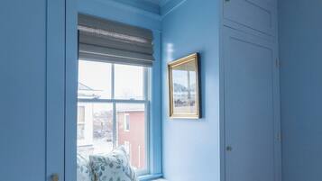 Quarto com um assento junto à janela, um quadro e uma porta.