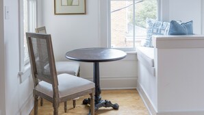 A room with a round table, a chair, a window with a view, and a framed botanical illustration on the wall. - Charming Downtown 2 BR Apartment Steps from Downtown Mall (Charlottesville)