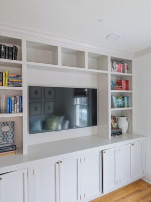 A room with a white entertainment unit, bookshelves, and a flat-screen TV.