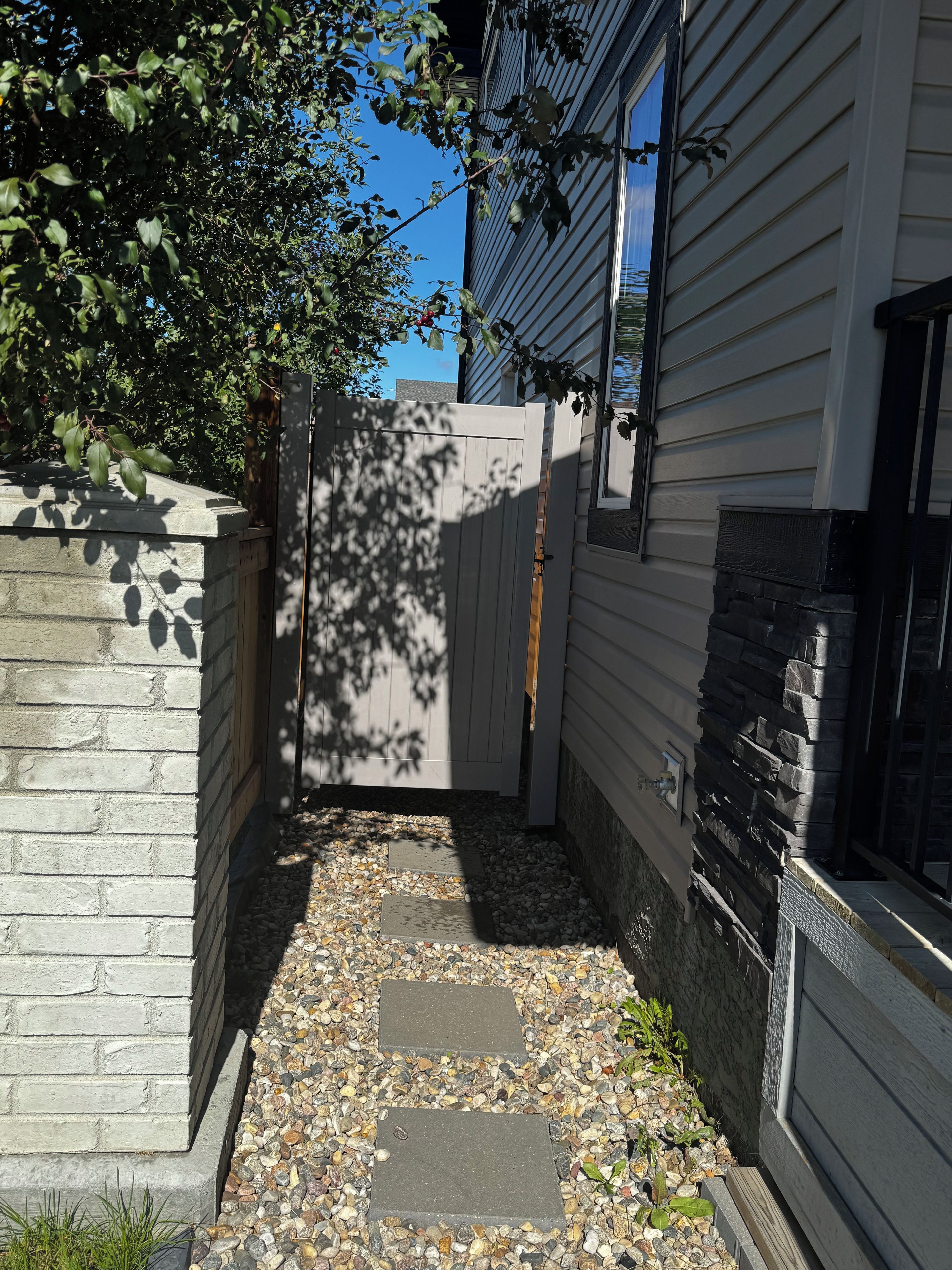 A narrow pathway with stepping stones leading to a gated area, flanked by a brick wall and a building with a stone accent.
