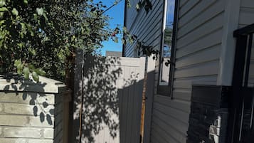 A narrow pathway with stepping stones leading to a gated area, flanked by a brick wall and a building with a stone accent.