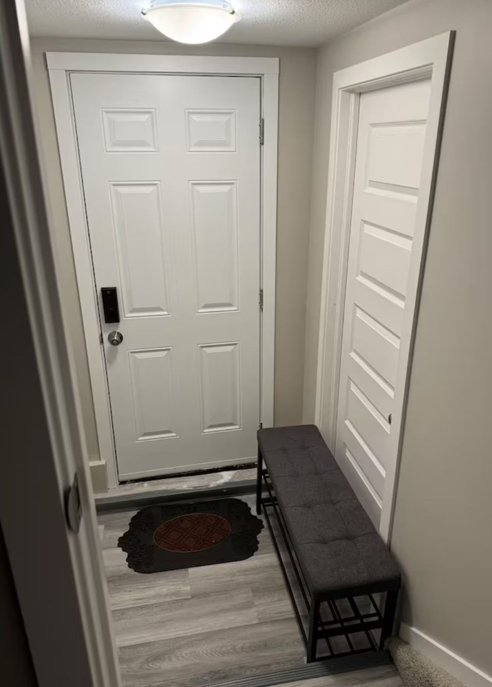 Un couloir avec une porte blanche, un banc et un tapis.