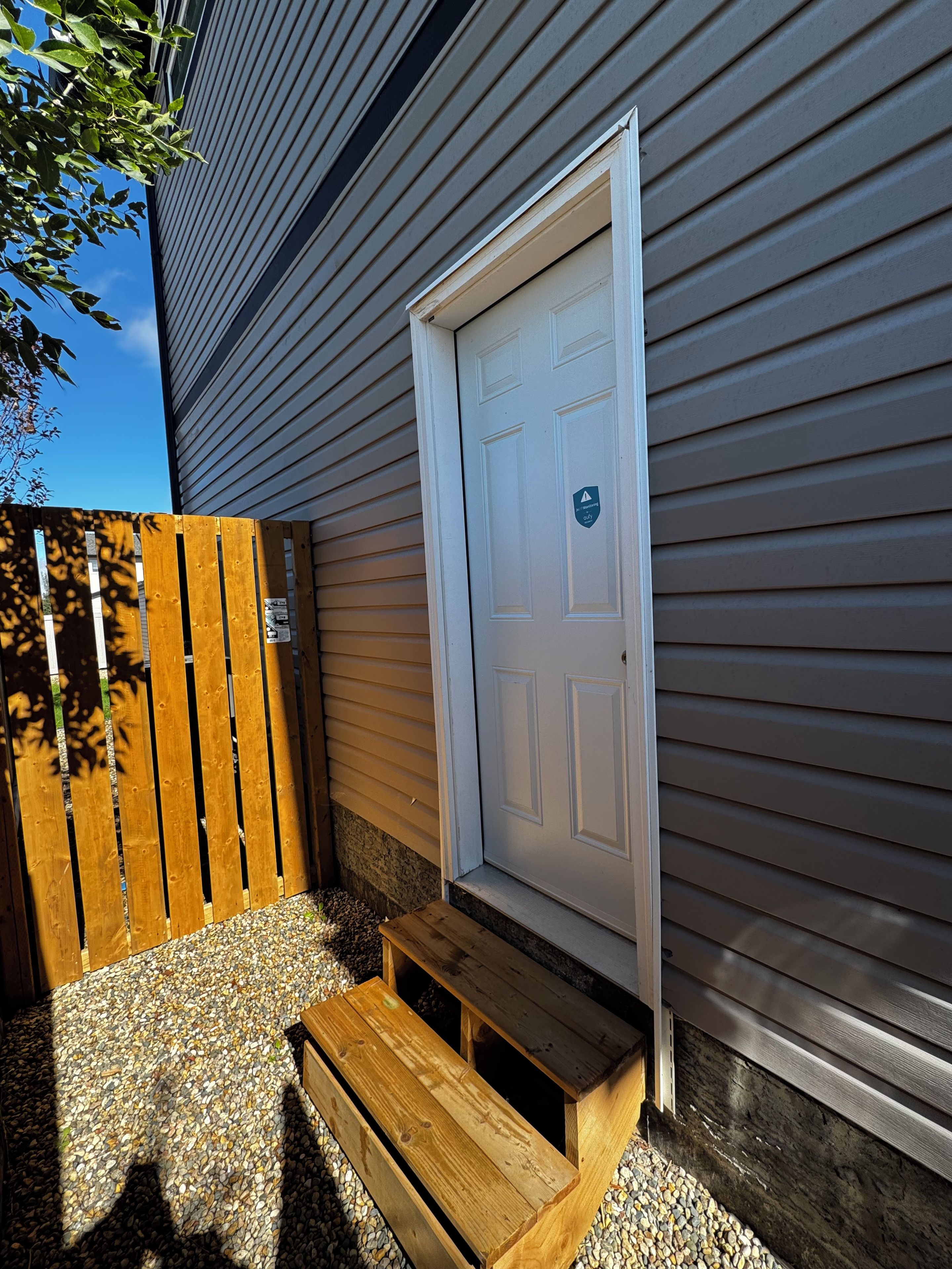 A wooden bench outside a house with a white door and a wooden fence.
