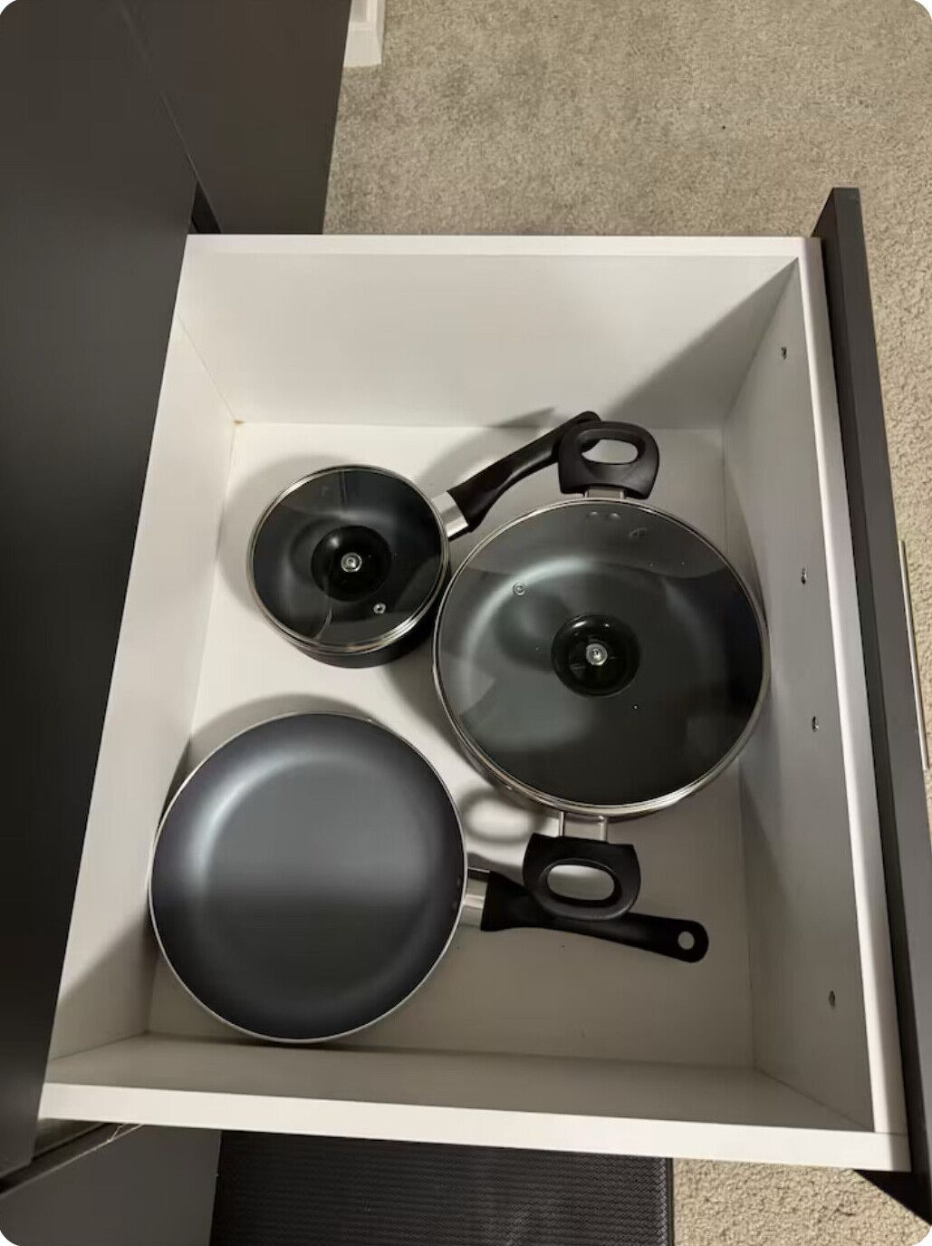 A kitchen drawer with three pots and pans.