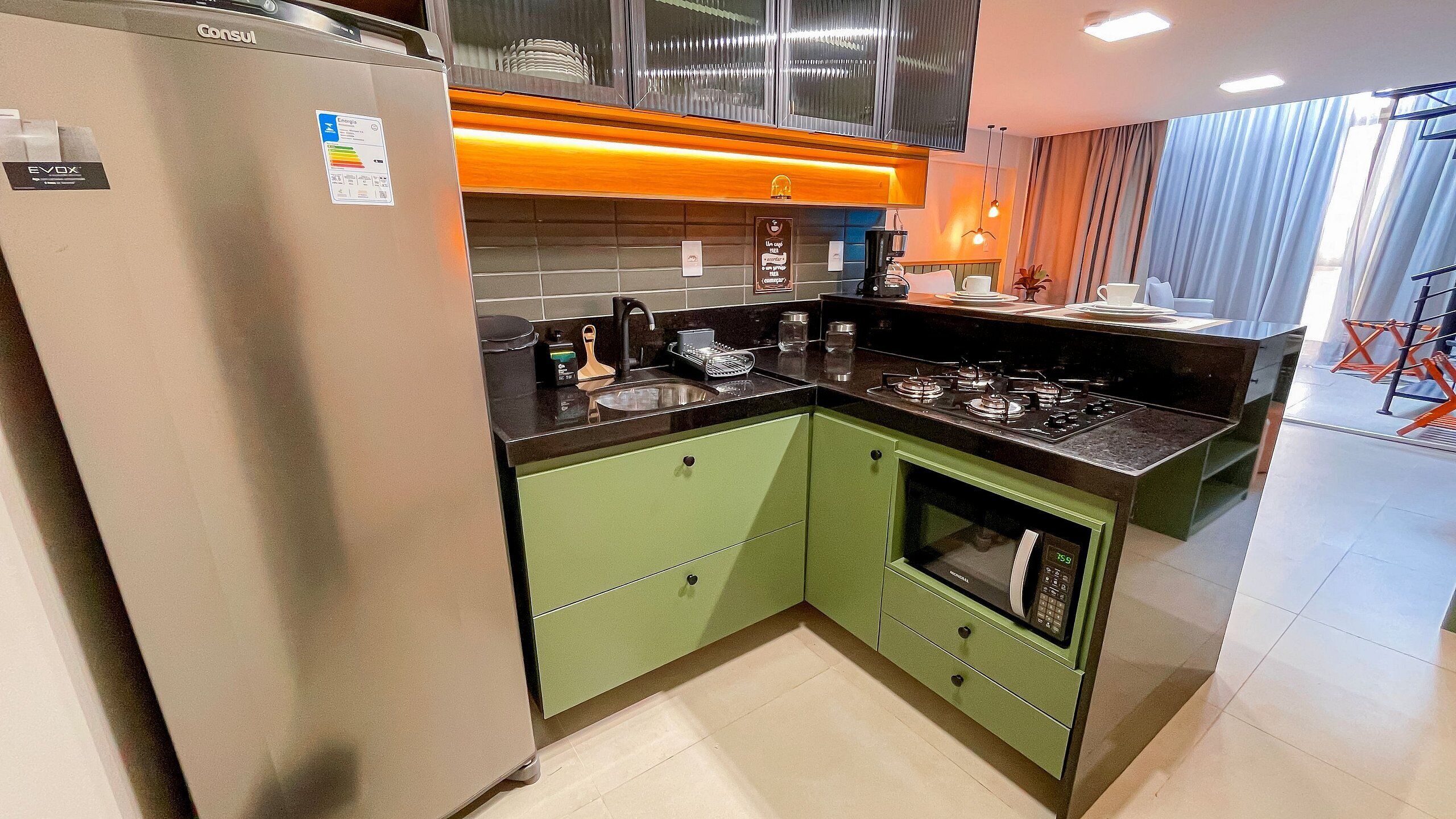 A modern kitchen with a stainless steel refrigerator, green cabinets, a built-in oven, and a gas stove.