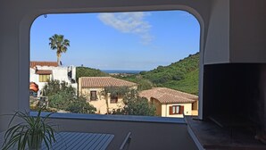Ein Balkon mit Blick auf eine Küstenlandschaft, darunter Häuser mit roten Ziegeldächern und eine Palme.