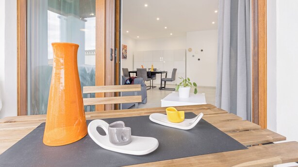 A modern dining area with a wooden table, a large orange vase, a white mug, and a yellow cup on a black placemat.