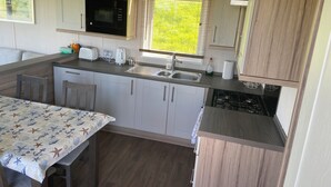 A compact kitchen with a microwave, toaster, sink, and a gas stove. - The Lodge at Pennant-igyn (Pwllheli)